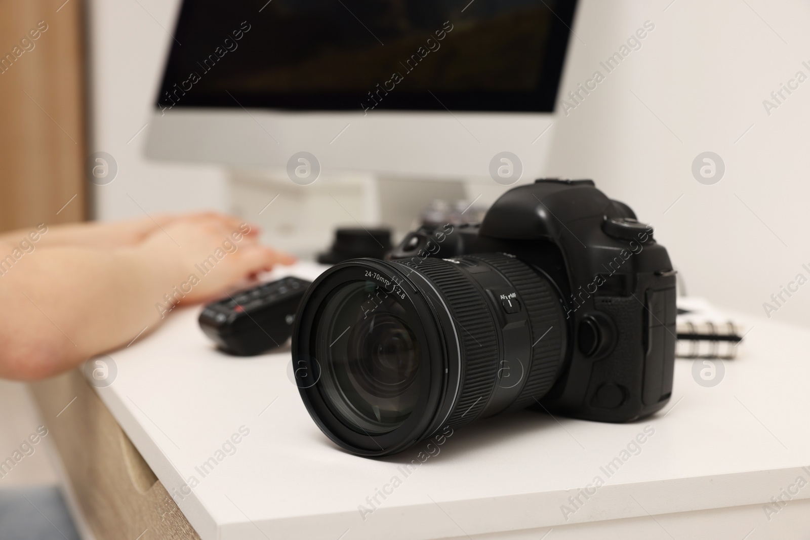 Photo of Photographer working on computer at white table with camera indoors, closeup