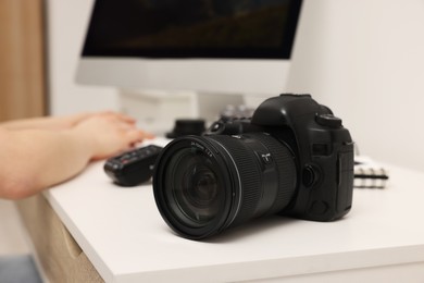 Photographer working on computer at white table with camera indoors, closeup