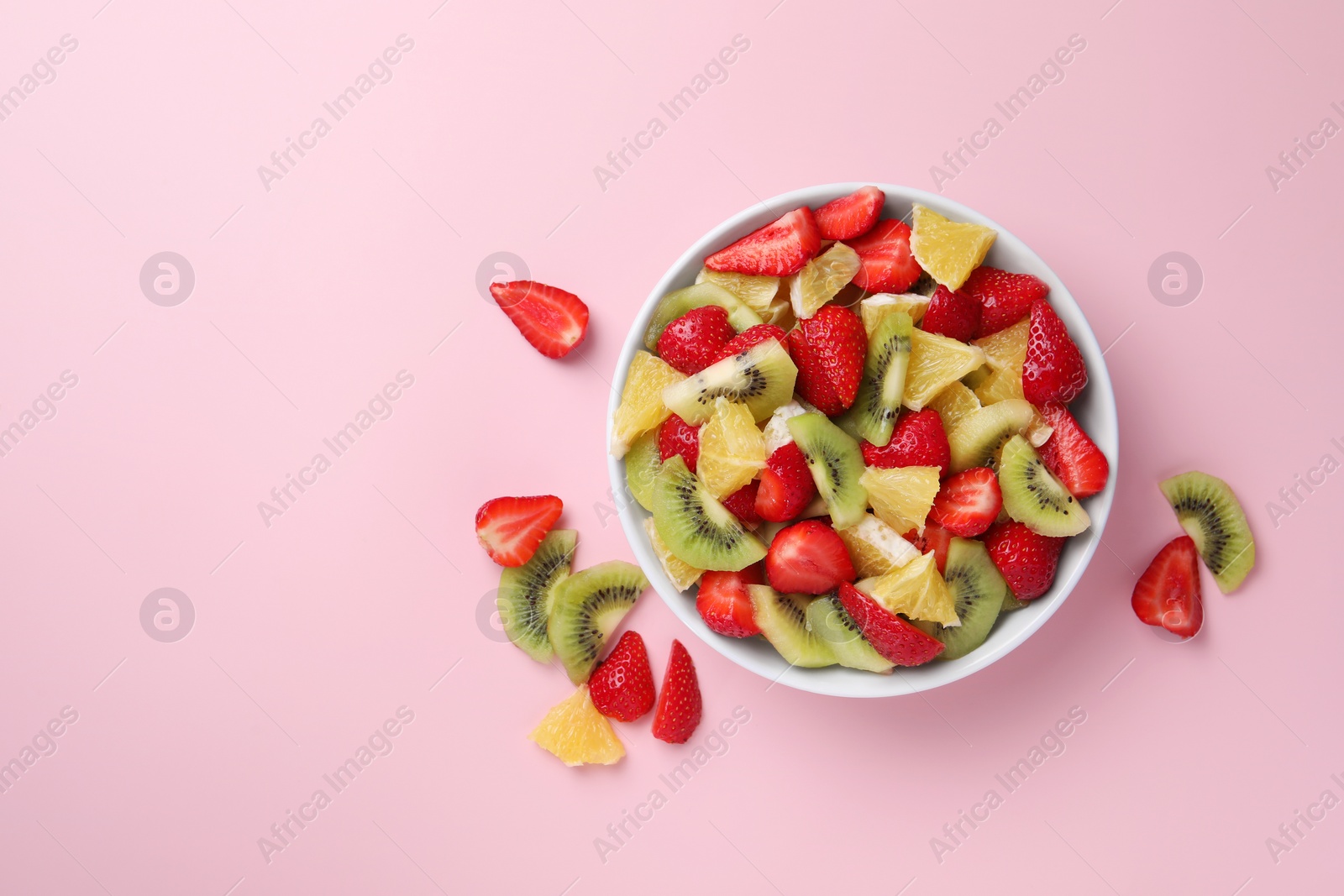Photo of Yummy fruit salad in bowl and ingredients on pink background,flat lay. Space for text