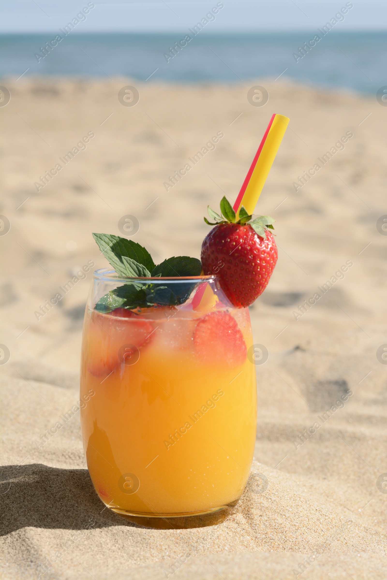 Photo of Glass of refreshing drink with strawberry on sandy beach near sea