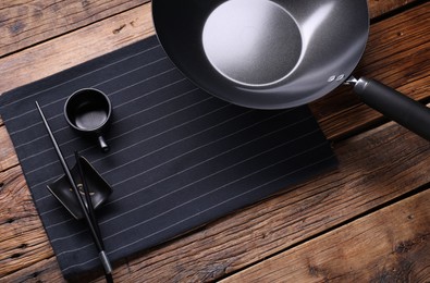 Empty iron wok, sauce bowl and chopsticks on wooden table