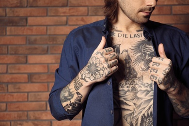 Young man with tattoos on body near brick wall, closeup