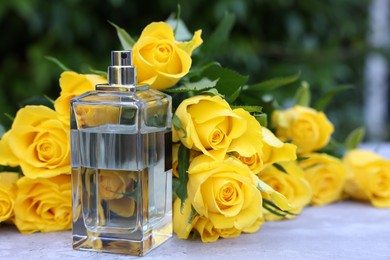 Photo of Perfume and beautiful bouquet of yellow roses on light table outdoors, closeup. Space for text