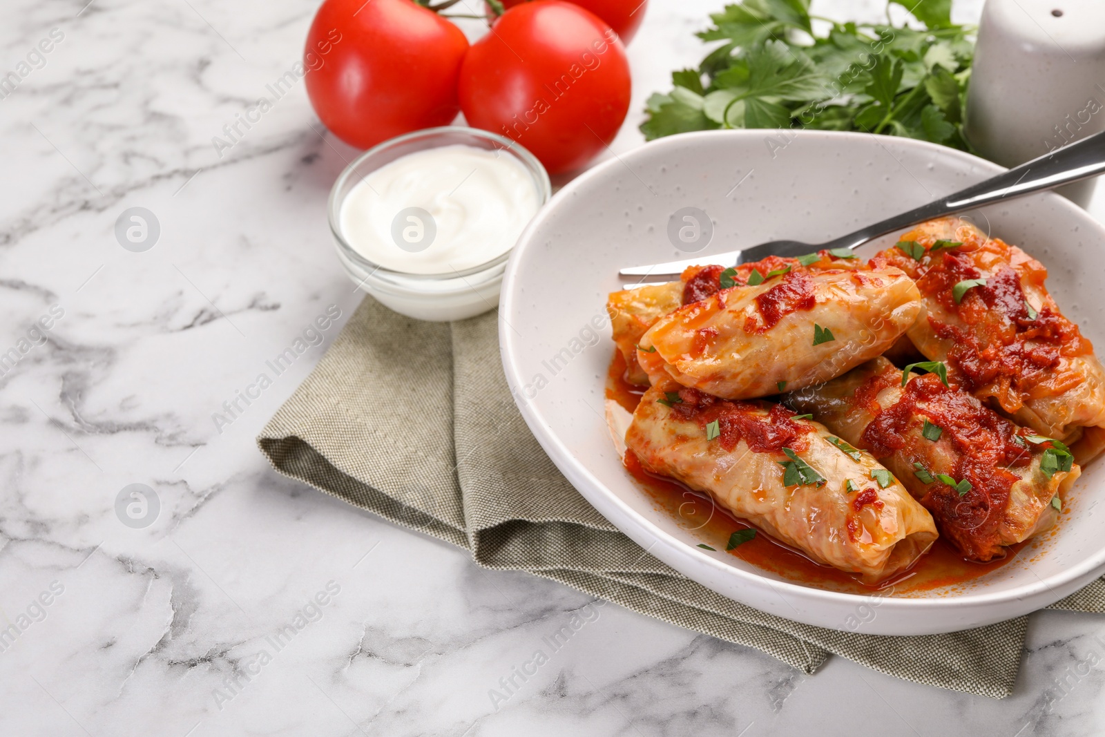 Photo of Delicious stuffed cabbage rolls cooked with homemade tomato sauce on white marble table, closeup. Space for text