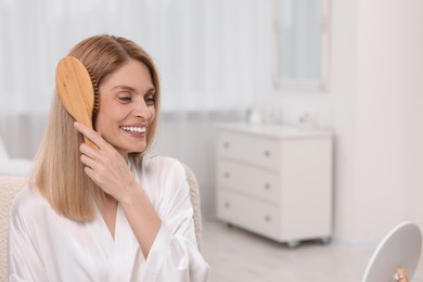 Photo of Beautiful happy woman brushing her hair near mirror in bedroom, space for text