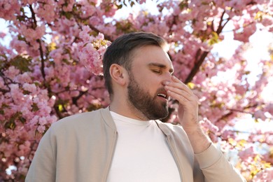 Photo of Man suffering from seasonal pollen allergy near blossoming tree outdoors