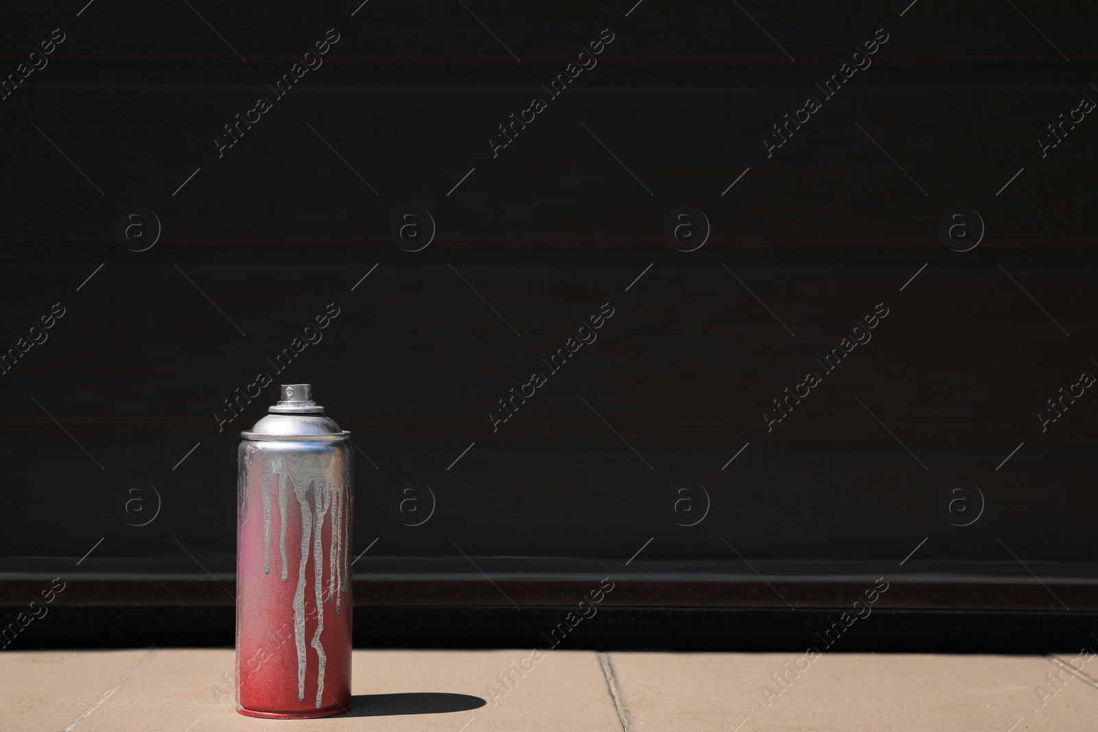 Photo of Used can of spray paint on tile floor near black wall outdoors, space for text. Graffiti supplies