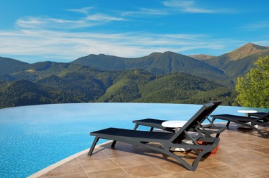 Image of Chaise longues near outdoor swimming pool at resort and beautiful view of mountains on sunny day