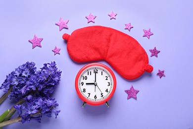 Photo of Soft sleep mask, decor in shape of stars, alarm clock and flowers on purple background, flat lay