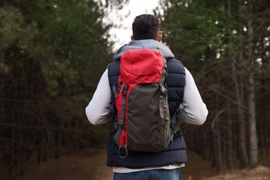 Photo of Man with backpack walking in forest, back view