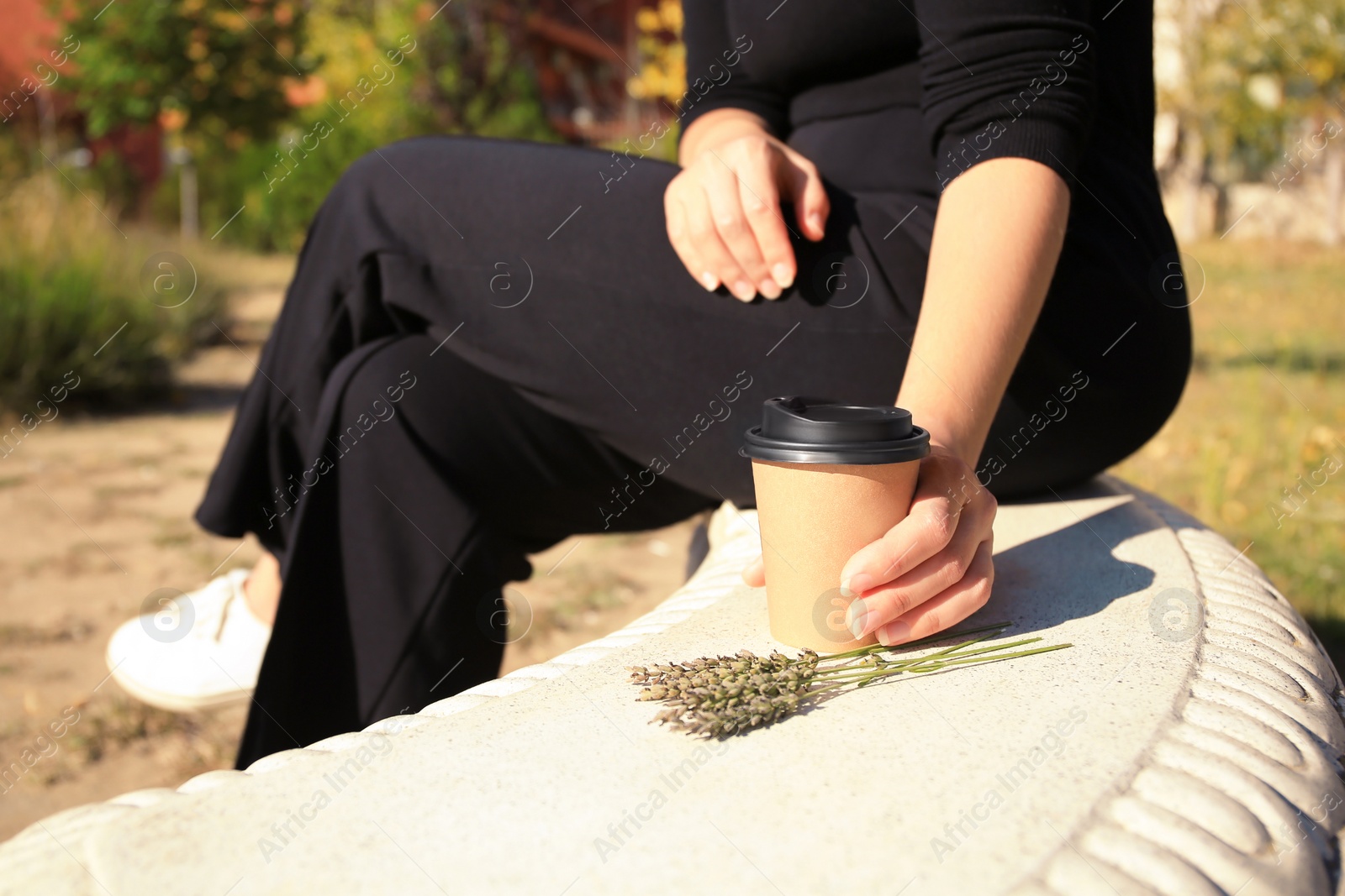 Photo of Woman with cardboard cup of coffee sitting on stone bench outdoors, closeup