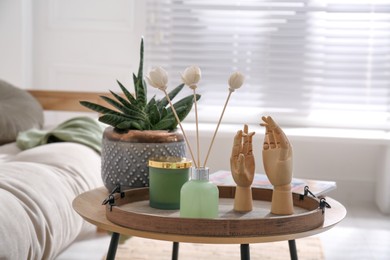 Photo of Wooden tray with air reed freshener, plant and mannequin hands on table in living room