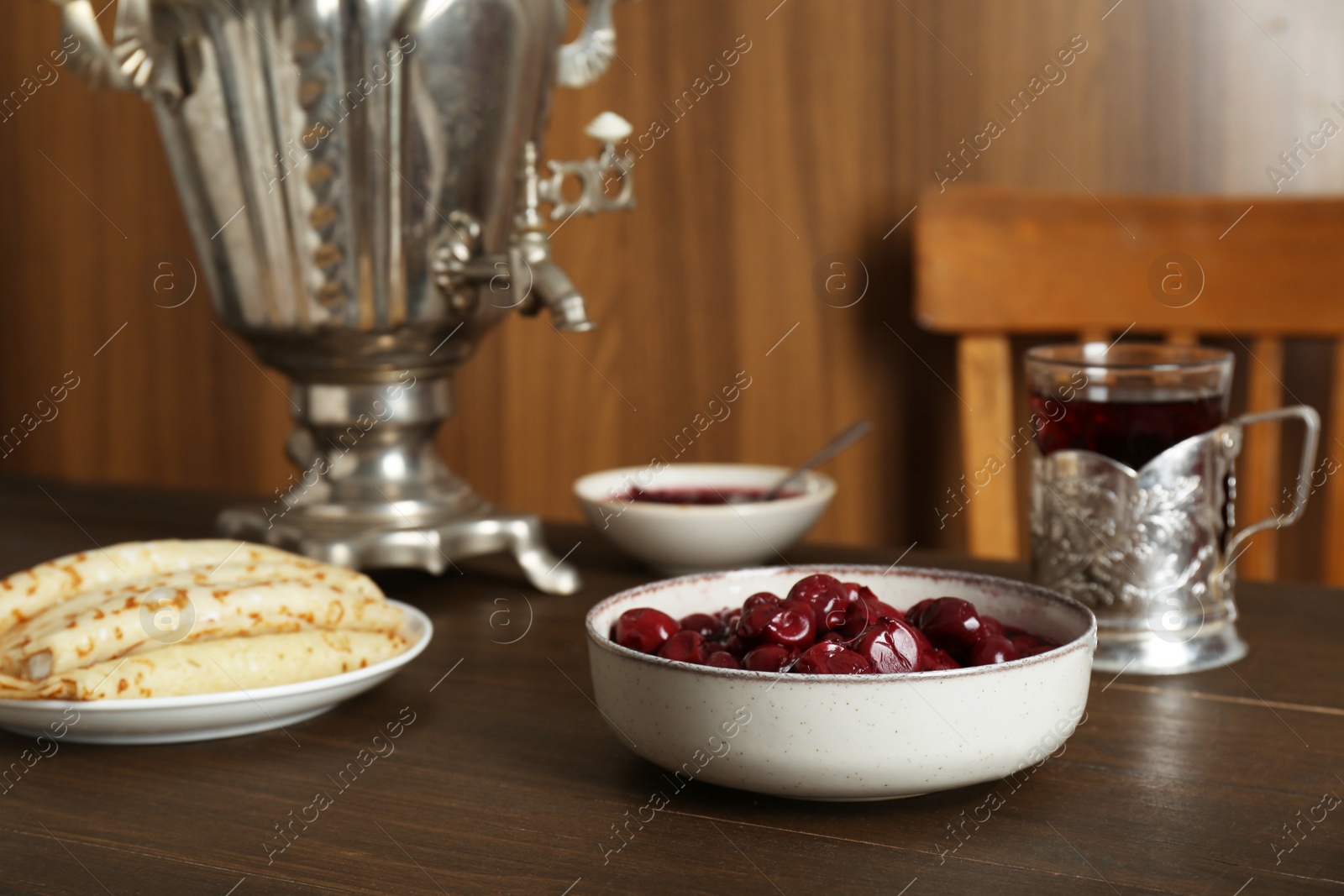 Photo of Vintage samovar, cup of hot drink and snacks served on wooden table. Traditional Russian tea ceremony