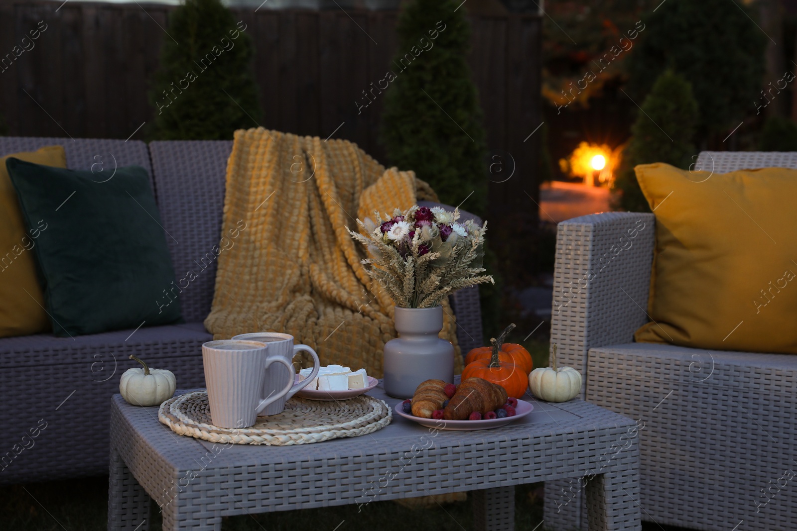 Photo of Cups of drink, cheese, croissants and autumn decor on table outdoors. Garden rattan furniture