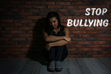 Message STOP BULLYING and abused teen girl crying near brick wall