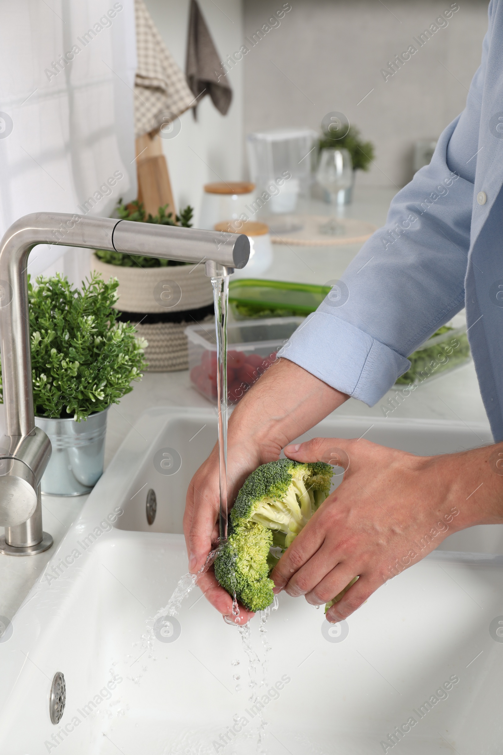 Photo of Man washing fresh broccoli in kitchen, closeup. Food storage