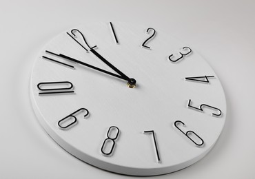 Photo of Stylish analog clock hanging on white wall. New Year countdown