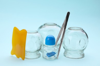 Photo of Glass cups and other equipment for cupping therapy on light blue background