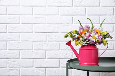 Photo of Watering can with beautiful wild flowers on table near brick wall