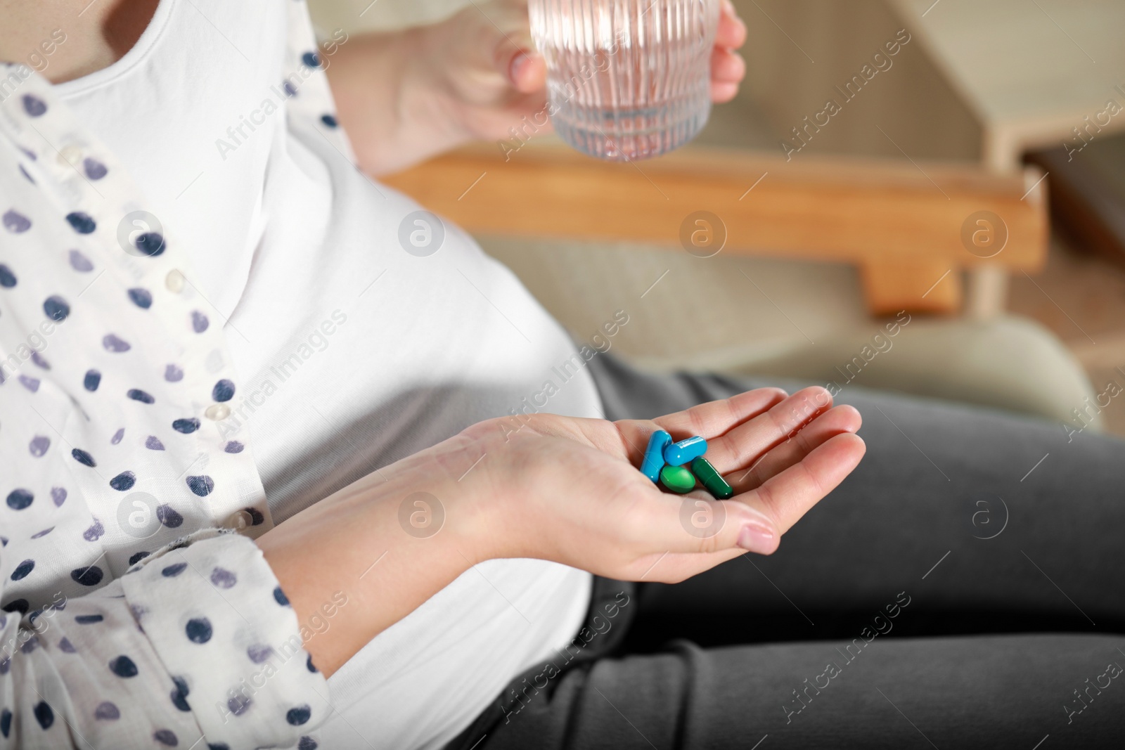 Photo of Pregnant woman holding pile of pills and glass with water indoors, closeup