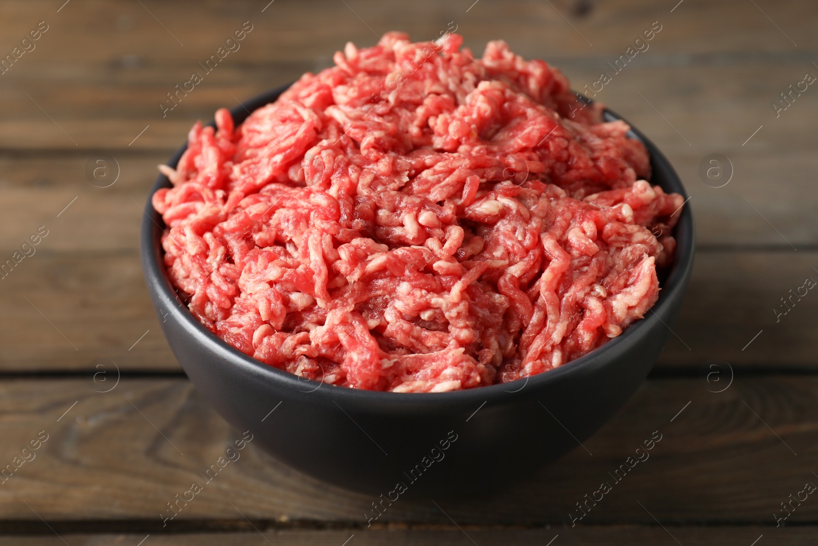 Photo of Raw ground meat in bowl on wooden table, closeup