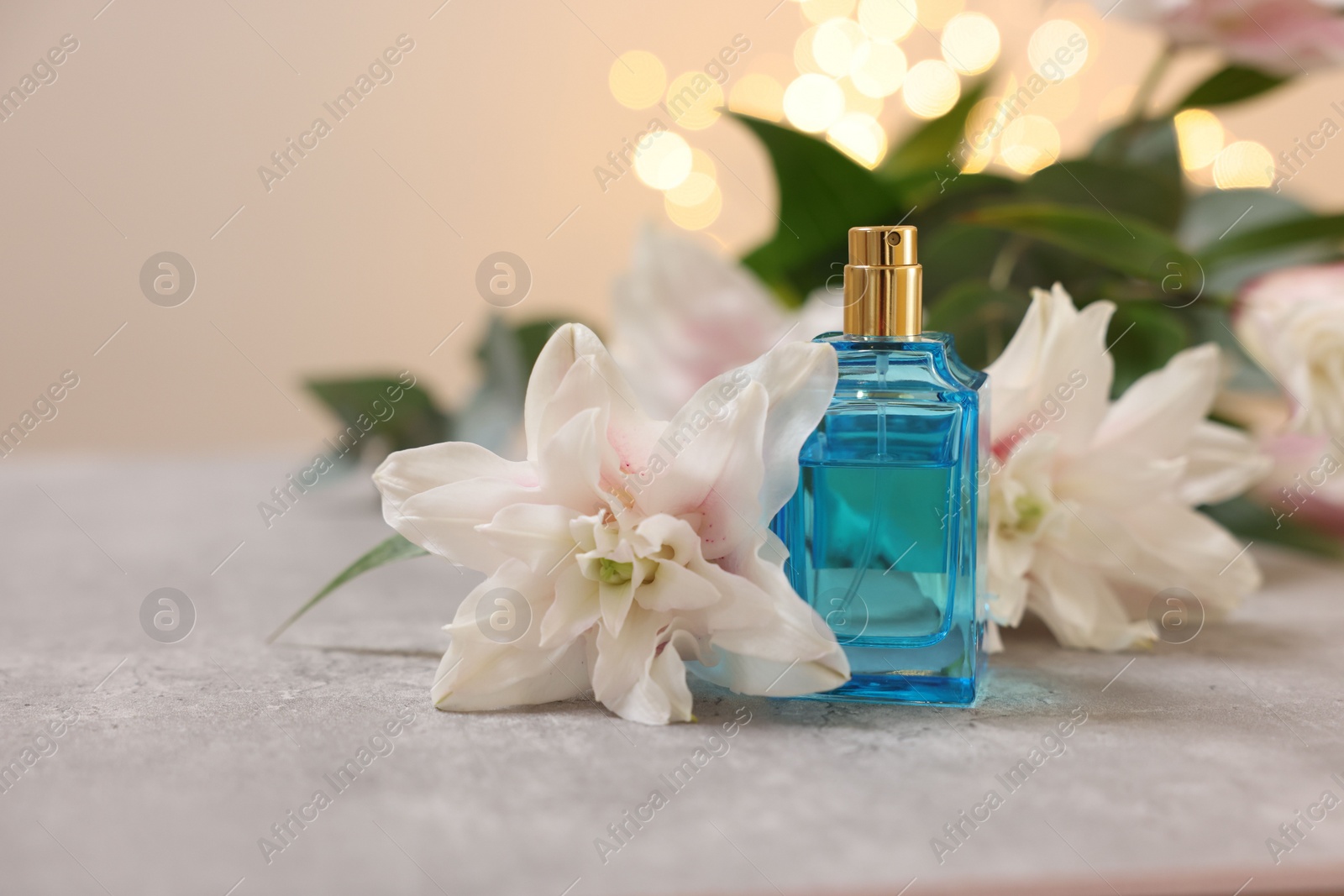 Photo of Bottle of perfume and beautiful lily flowers on table against beige background with blurred lights, closeup. Space for text