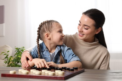 Photo of Playing checkers. Mother learning her daughter at table in room