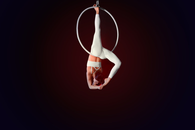 Photo of Young woman performing acrobatic element on aerial ring indoors