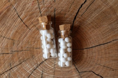 Photo of Bottles with homeopathic remedy on wooden stump, flat lay