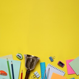 Different stationery and school bell on yellow background, flat lay. Space for text