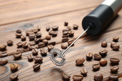 Photo of Black milk frother wand and coffee beans on wooden table, closeup