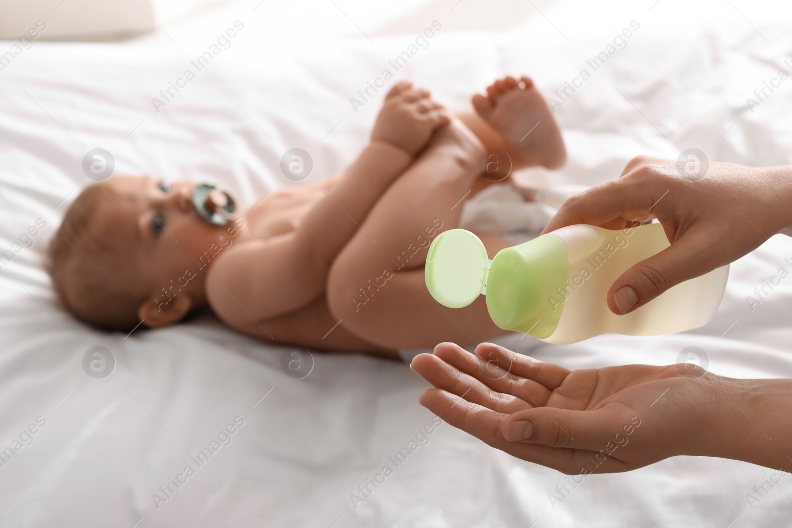 Photo of Mother with bottle of massage oil near baby on bed, closeup