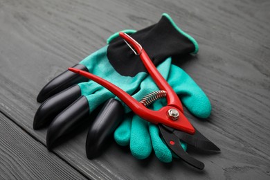 Photo of Pair of claw gardening gloves and secateurs on grey wooden table, closeup