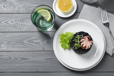 Photo of Delicious black risotto with baby octopus served on grey wooden table, flat lay