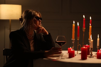 Photo of Beautiful young woman with sunglasses and glass of wine at table in restaurant