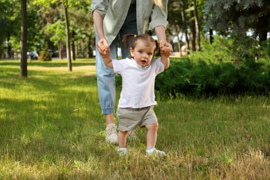 Mother supporting daughter while she learning to walk in park, closeup