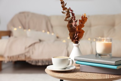 Photo of Burning candle, cup and books on wooden coffee table in room. Space for text