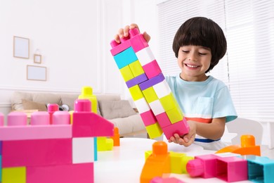 Photo of Cute little boy playing with colorful building blocks at table in living room