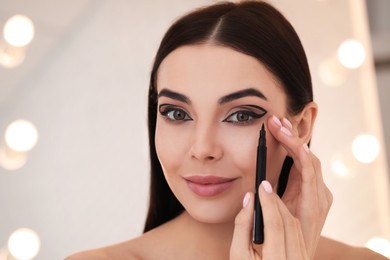 Beautiful young woman applying black eyeliner indoors