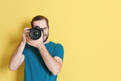 Young photographer with professional camera on color background