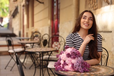 Photo of Beautiful woman with bouquet of spring flowers in outdoor cafe, space for text
