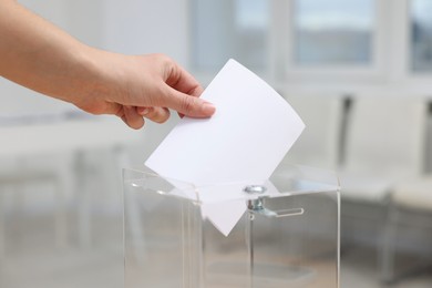 Photo of Woman putting her vote into ballot box on blurred background, closeup