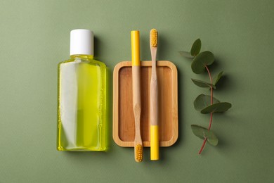 Fresh mouthwash in bottle, toothbrushes and eucalyptus branch on green background, flat lay