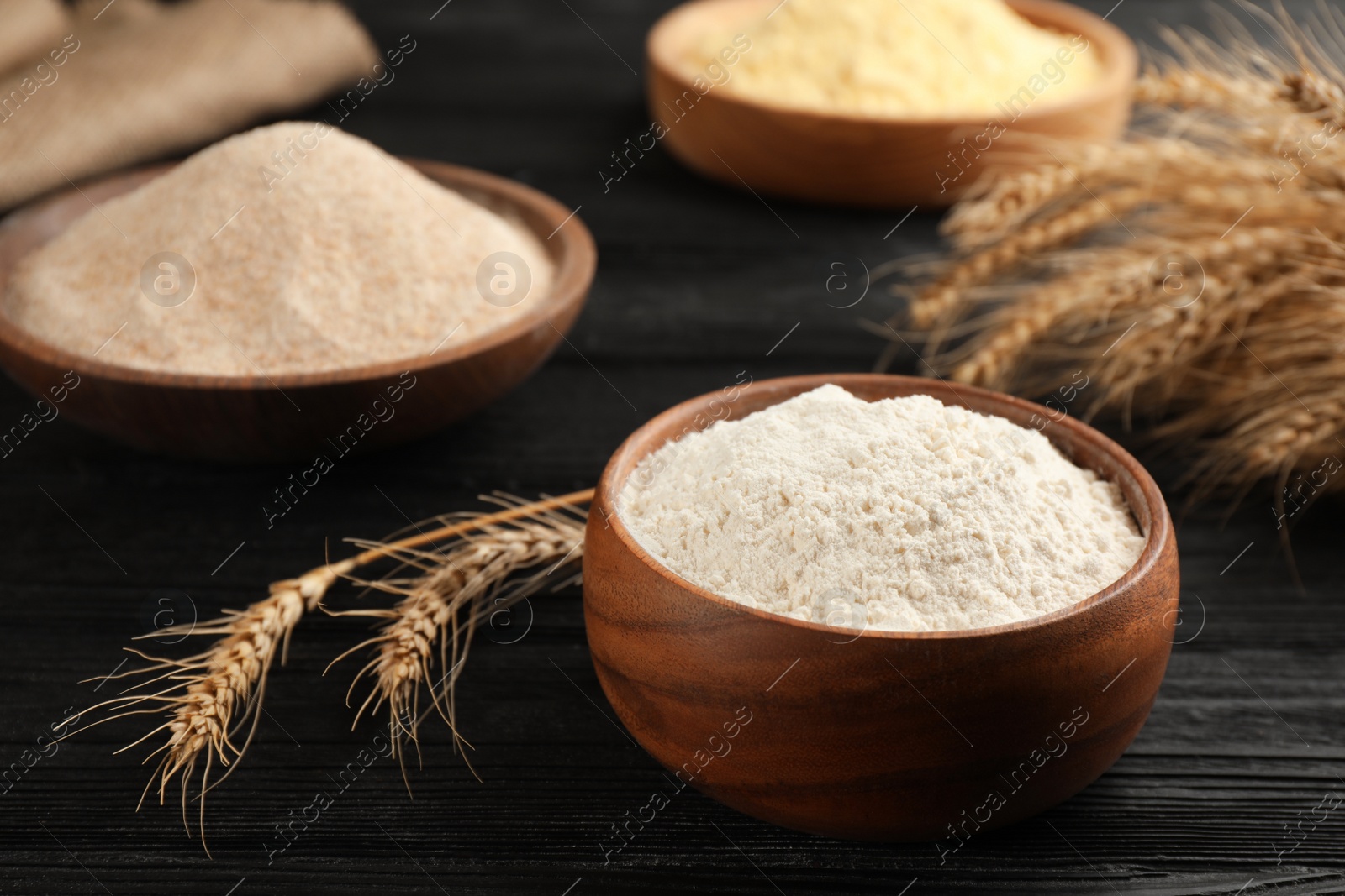 Photo of Bowl of flour and wheat ears on black wooden table