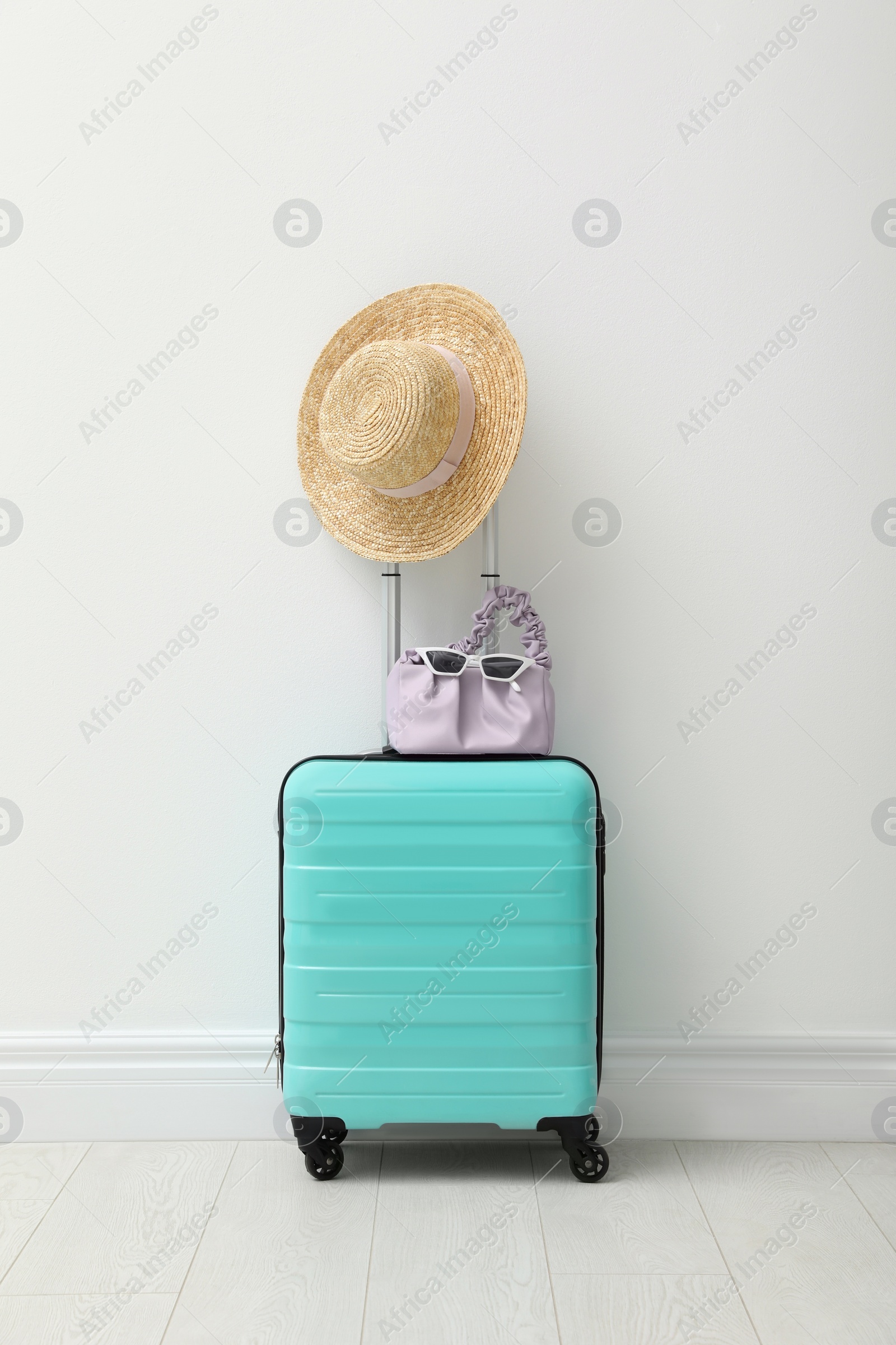 Photo of Suitcase packed for trip and summer accessories near white wall indoors