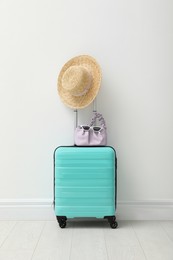 Suitcase packed for trip and summer accessories near white wall indoors