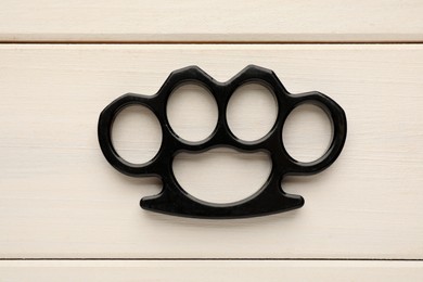 Photo of Black brass knuckles on white wooden background, top view