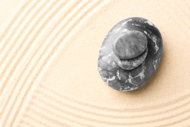 Photo of Zen garden stones on beige sand with pattern, top view. Space for text