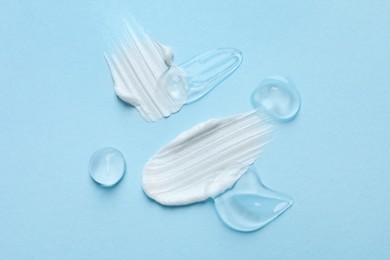 Photo of Samples of cosmetic gel and cream on light blue background, top view