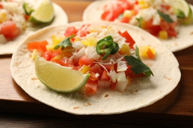 Photo of Delicious tacos with vegetables, lime and parsley on wooden table, closeup